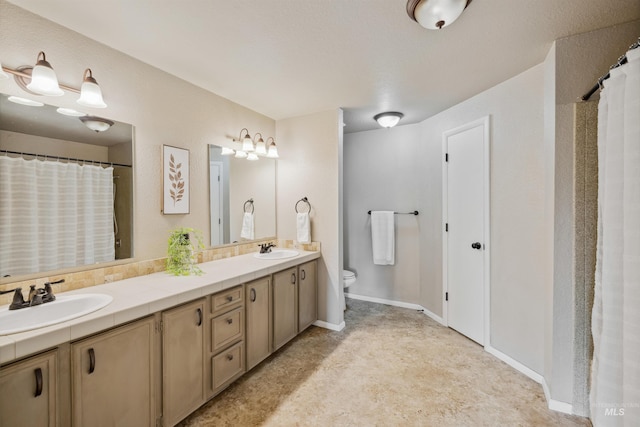 bathroom featuring toilet, double vanity, baseboards, and a sink