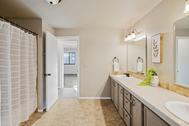 bathroom with tile patterned floors, a sink, baseboards, and double vanity