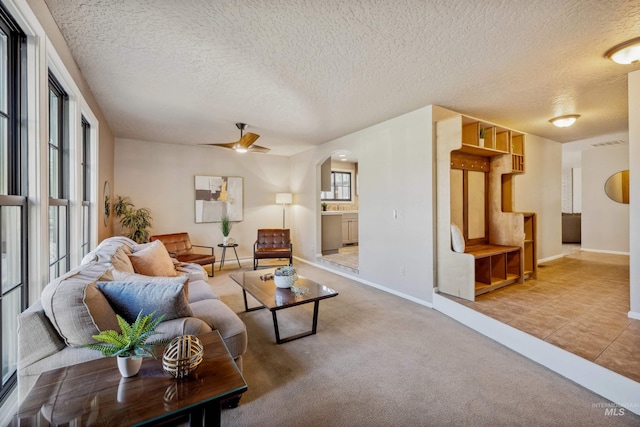 carpeted living area with arched walkways, ceiling fan, a textured ceiling, baseboards, and tile patterned floors