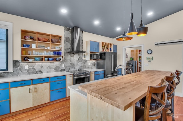 2809 Hampton Ct, Moscow, ID 83843 - kitchen with wall chimney exhaust hood, appliances with stainless steel finishes, light wood-style floors, decorative backsplash, and blue cabinets