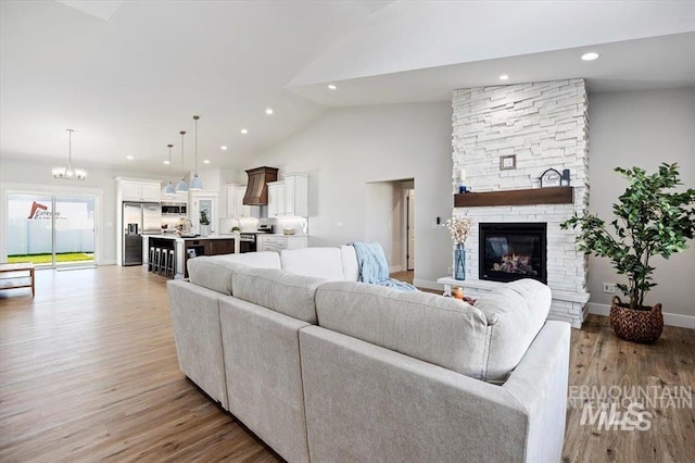 living room featuring an inviting chandelier, a fireplace, light hardwood / wood-style flooring, and high vaulted ceiling