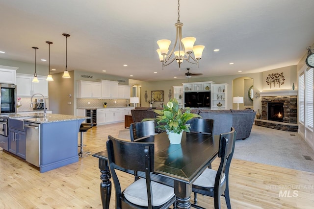 3214 S Arctic Fox Ave, Eagle, ID 83616 - dining space featuring a chandelier, light wood-style flooring, arched walkways, a stone fireplace, and recessed lighting
