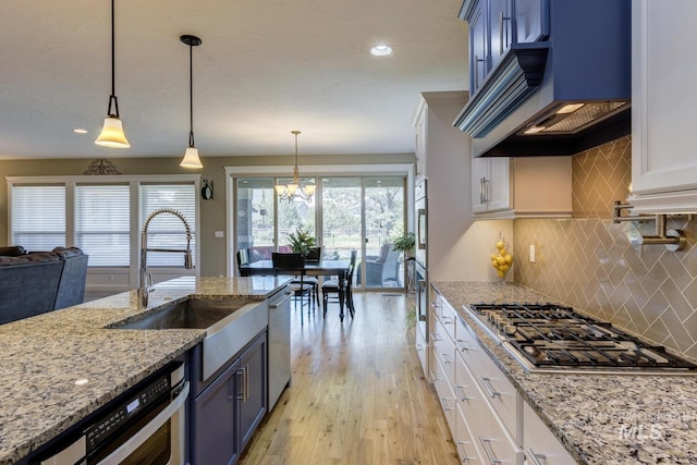 3214 S Arctic Fox Ave, Eagle, ID 83616 - kitchen featuring stainless steel appliances, custom exhaust hood, blue cabinets, light wood-type flooring, and decorative backsplash