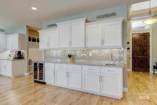 3214 S Arctic Fox Ave, Eagle, ID 83616 - kitchen with wine cooler, white cabinets, light wood-style floors, tasteful backsplash, and recessed lighting