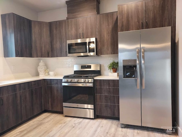 kitchen with dark brown cabinetry, stainless steel appliances, light wood-type flooring, and backsplash