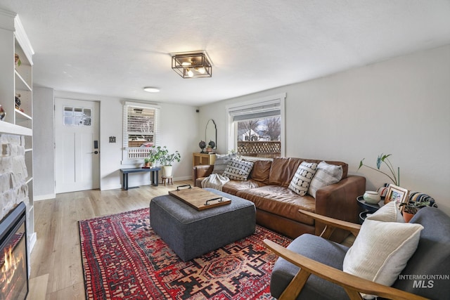 living room featuring a stone fireplace, light wood-type flooring, and baseboards