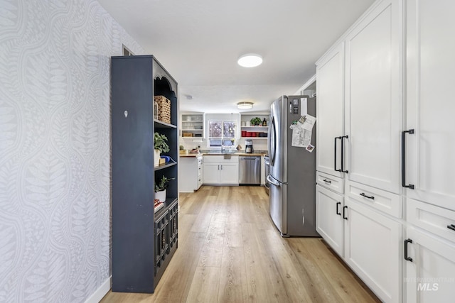 kitchen with light wood finished floors, open shelves, appliances with stainless steel finishes, white cabinets, and a sink