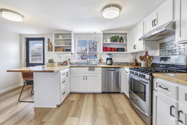 kitchen with a peninsula, stainless steel appliances, under cabinet range hood, open shelves, and a sink