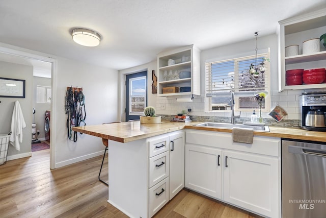 kitchen with open shelves, wooden counters, stainless steel dishwasher, a sink, and a peninsula