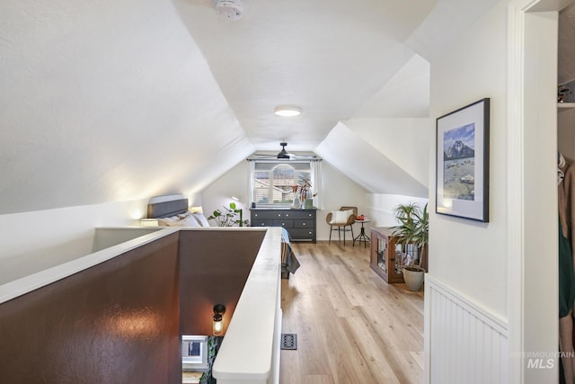 bedroom featuring light wood-style floors, lofted ceiling, and a wainscoted wall