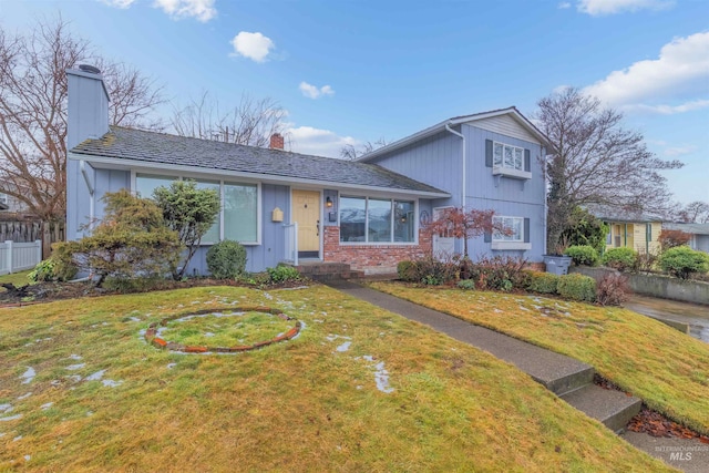 tri-level home with a front yard, brick siding, fence, and a chimney