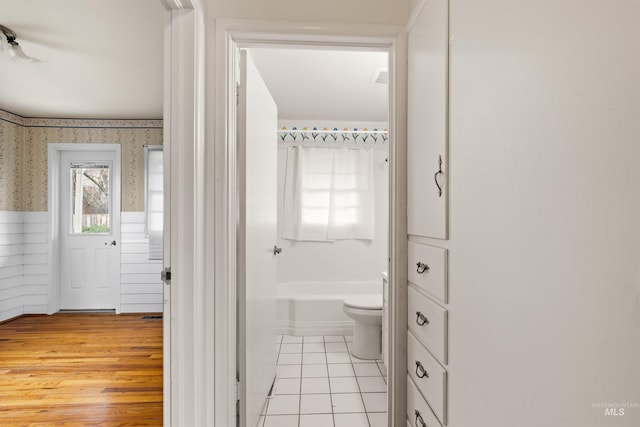 full bathroom featuring wallpapered walls, wainscoting, toilet, a bathing tub, and wood finished floors