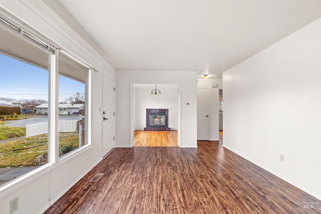 unfurnished living room featuring a brick fireplace, baseboards, visible vents, and wood finished floors