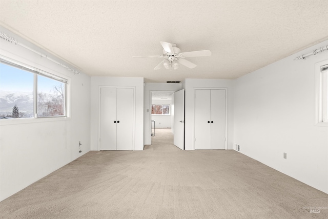 unfurnished bedroom featuring light carpet, a textured ceiling, visible vents, and multiple closets