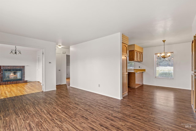 unfurnished living room with baseboards, dark wood finished floors, a notable chandelier, and a tile fireplace