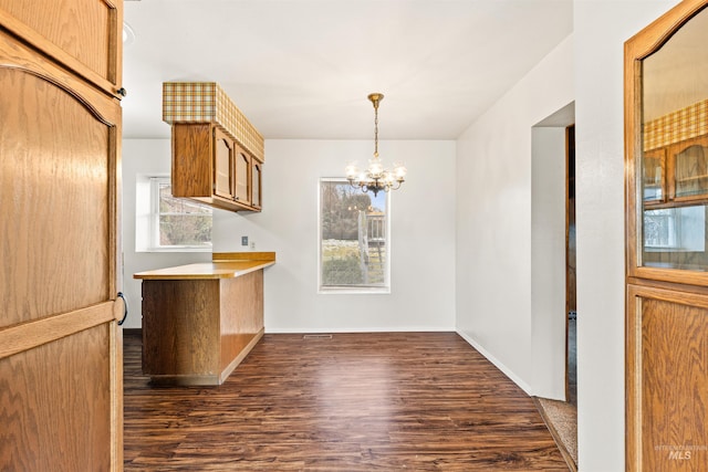 kitchen with hanging light fixtures, an inviting chandelier, a peninsula, and dark wood-type flooring