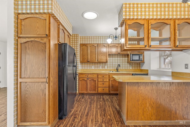 kitchen with a peninsula, dark wood-type flooring, a sink, light countertops, and black appliances