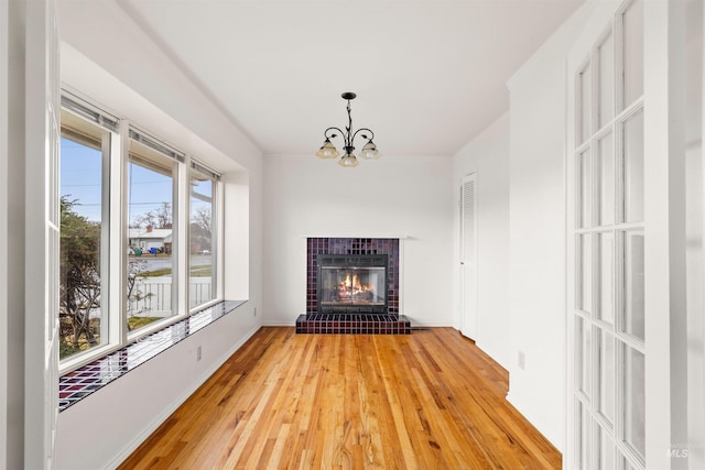 unfurnished living room featuring crown molding, light wood finished floors, a fireplace, and an inviting chandelier