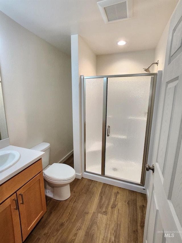 bathroom with wood-type flooring, a shower with door, vanity, and toilet