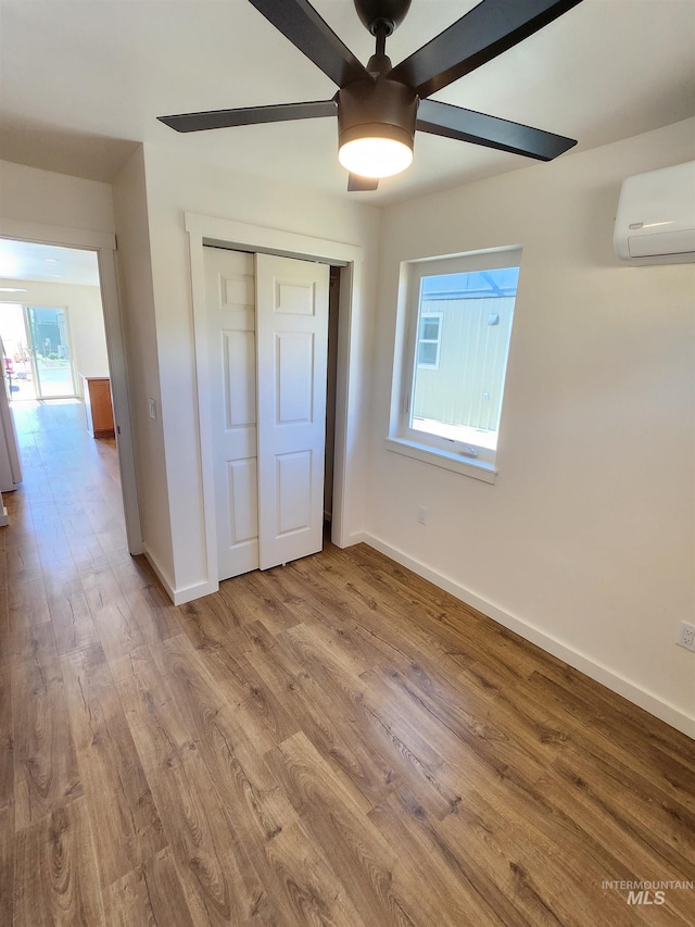 unfurnished bedroom featuring ceiling fan, a closet, light wood-type flooring, and a wall mounted AC