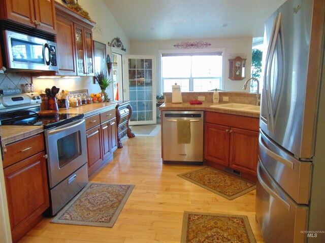 kitchen with light wood-type flooring, backsplash, vaulted ceiling, sink, and stainless steel appliances