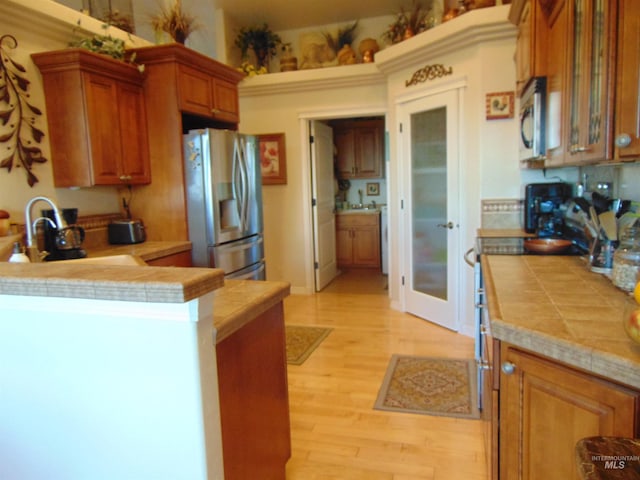 kitchen with appliances with stainless steel finishes, sink, light wood-type flooring, tile counters, and kitchen peninsula