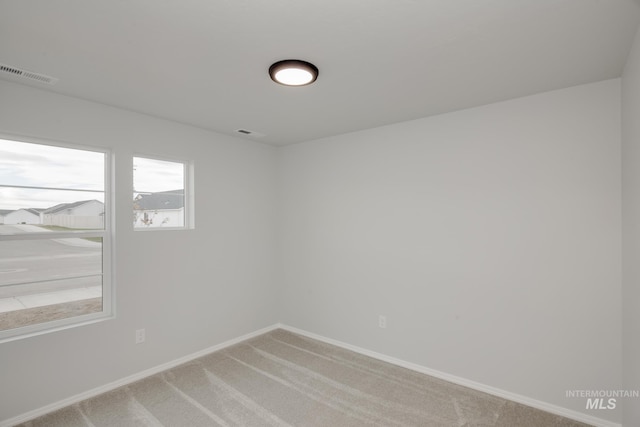 empty room with baseboards, visible vents, and light carpet