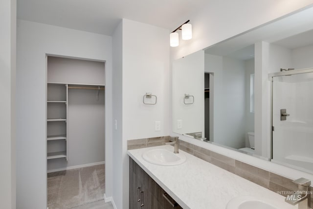 bathroom featuring double vanity, a stall shower, a sink, a spacious closet, and toilet