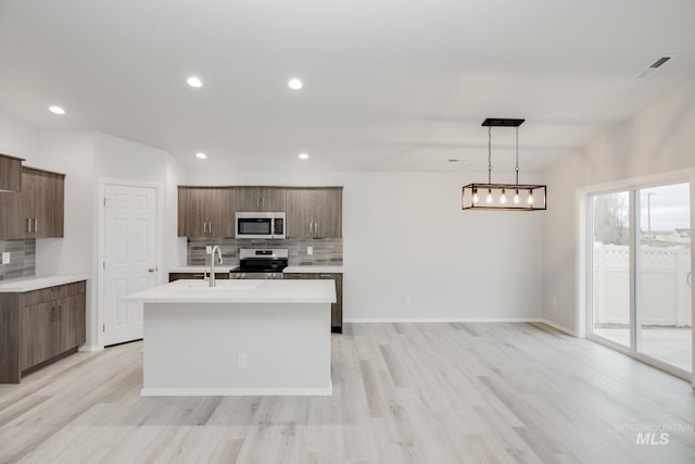 kitchen featuring an island with sink, decorative backsplash, stainless steel appliances, and light countertops