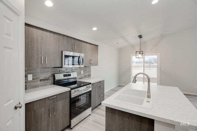 kitchen with tasteful backsplash, light countertops, an island with sink, stainless steel appliances, and a sink