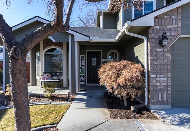 view of exterior entry with a shingled roof, covered porch, and an attached garage