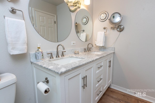 bathroom with double vanity, wood finished floors, a sink, and toilet