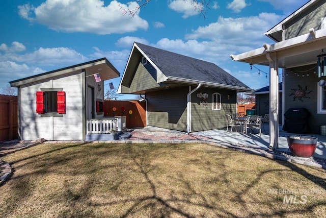 view of side of home with a patio, roof with shingles, fence, a yard, and an outdoor structure