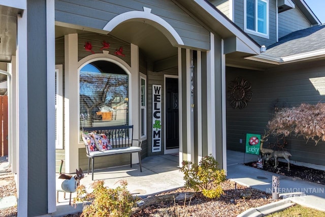 property entrance featuring covered porch and a shingled roof