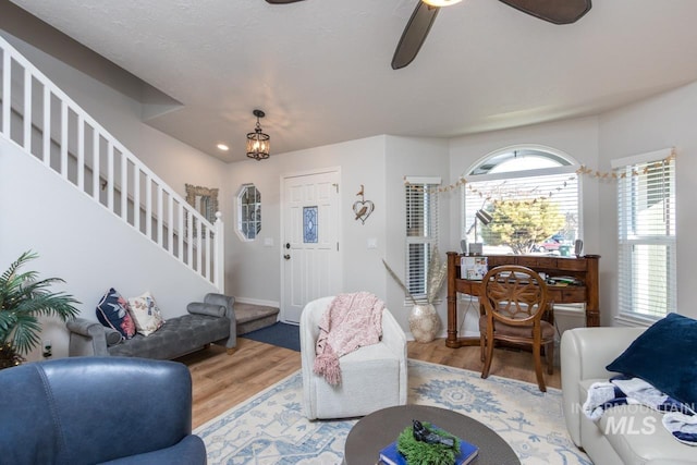 living area featuring light wood-style floors, ceiling fan with notable chandelier, baseboards, and stairs