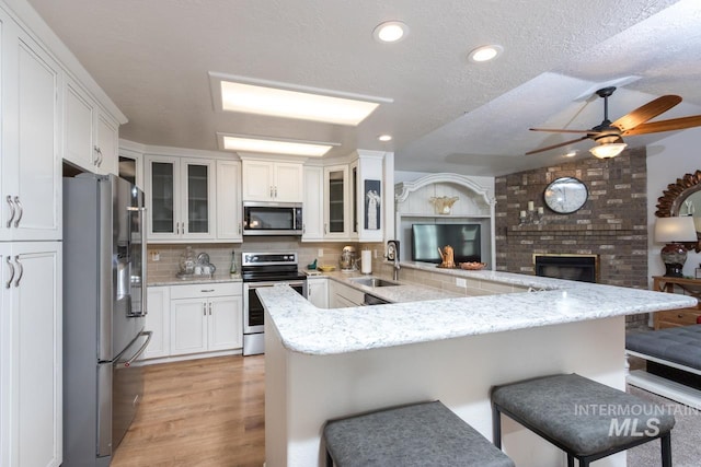 kitchen featuring decorative backsplash, a breakfast bar area, stainless steel appliances, a brick fireplace, and a sink