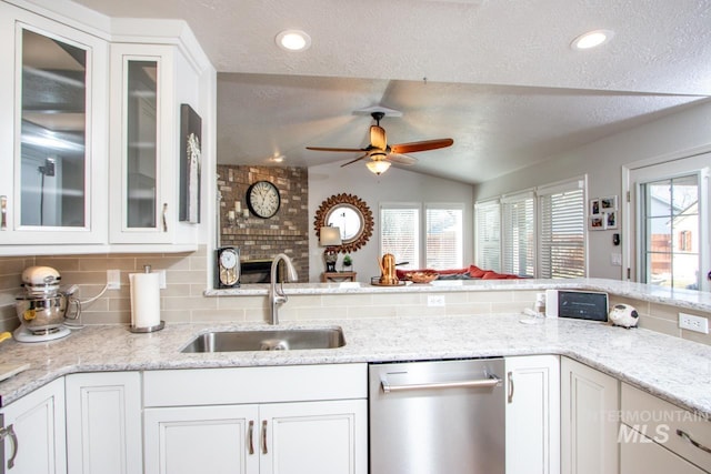 kitchen with tasteful backsplash, lofted ceiling, white cabinets, a sink, and dishwasher