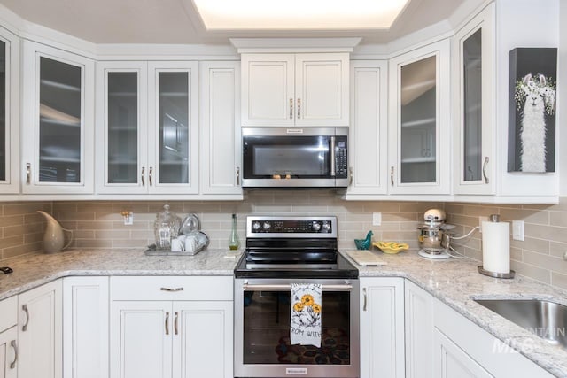 kitchen featuring light stone counters, decorative backsplash, appliances with stainless steel finishes, glass insert cabinets, and white cabinets