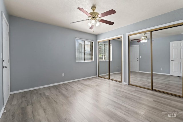 unfurnished bedroom featuring a ceiling fan, a textured ceiling, wood finished floors, baseboards, and two closets