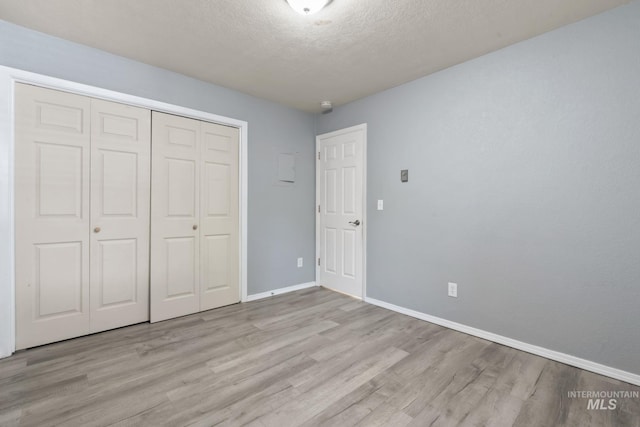 unfurnished bedroom featuring a closet, a textured ceiling, baseboards, and wood finished floors
