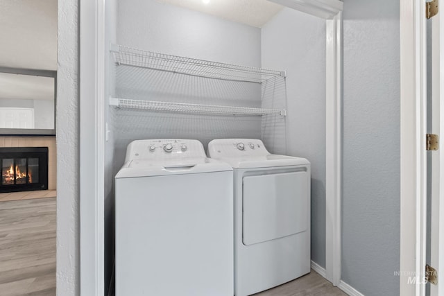 clothes washing area featuring laundry area, wood finished floors, a glass covered fireplace, a textured wall, and washer and clothes dryer