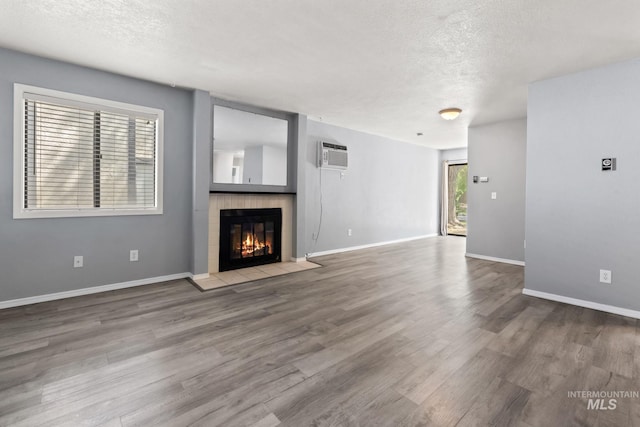 unfurnished living room with a textured ceiling, a glass covered fireplace, wood finished floors, and a wall mounted air conditioner