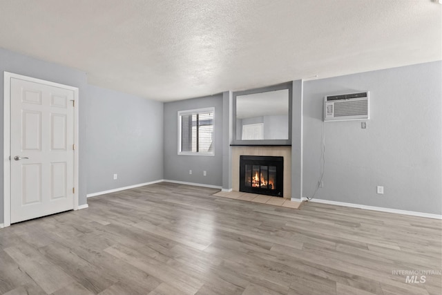 unfurnished living room with a textured ceiling, a fireplace with flush hearth, a wall mounted air conditioner, baseboards, and light wood-style floors
