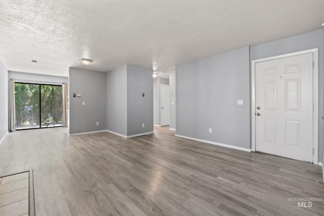 unfurnished living room featuring baseboards, a textured ceiling, and wood finished floors