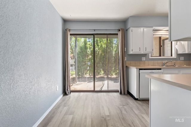 kitchen featuring white dishwasher, light wood-type flooring, light countertops, a textured wall, and white cabinetry