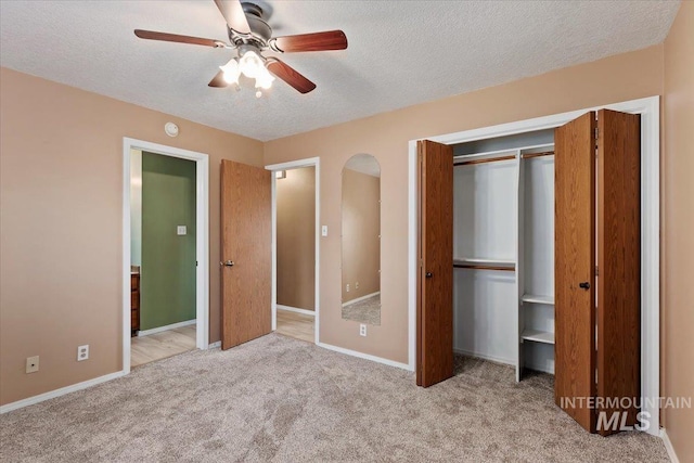 unfurnished bedroom with light carpet, ceiling fan, a closet, and a textured ceiling