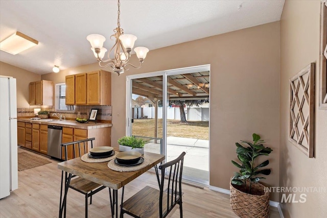 dining space with lofted ceiling, sink, a notable chandelier, and light hardwood / wood-style flooring