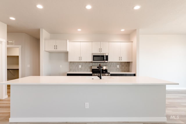 kitchen with appliances with stainless steel finishes, white cabinets, a large island with sink, and decorative backsplash