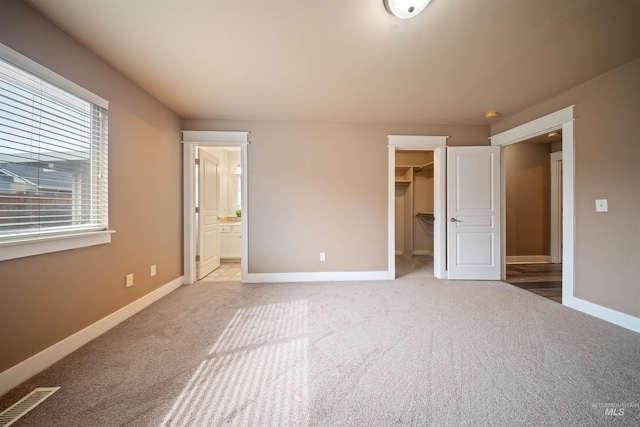 unfurnished bedroom featuring a spacious closet, baseboards, and light colored carpet