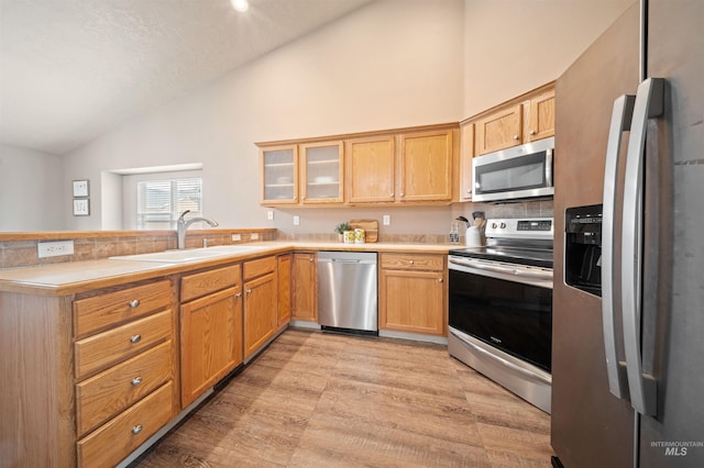 kitchen with a peninsula, appliances with stainless steel finishes, light countertops, and a sink